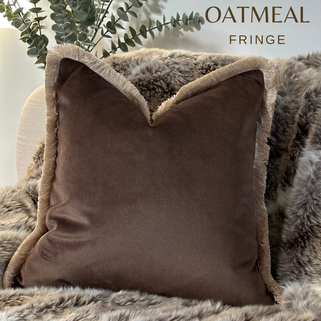 Luxury chocolate brown velvet pillow with a fringed trim in a neutral Living room on a cosy fur throw.