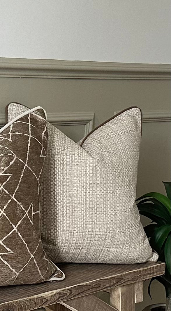 Cream woven pillow with beige piping trim.