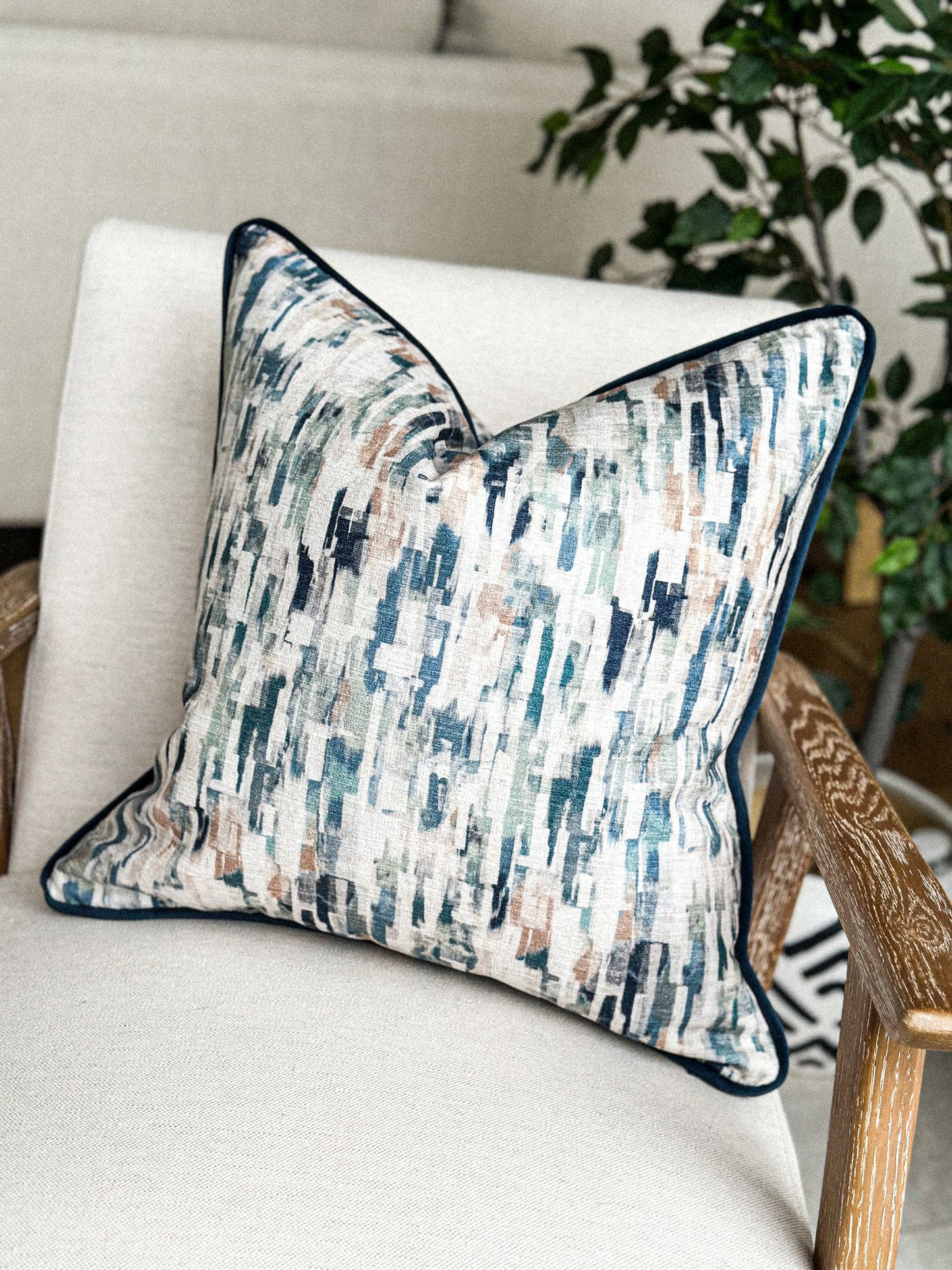 Painterly blue and sage cushion with piped edging on a neutral armchair.”