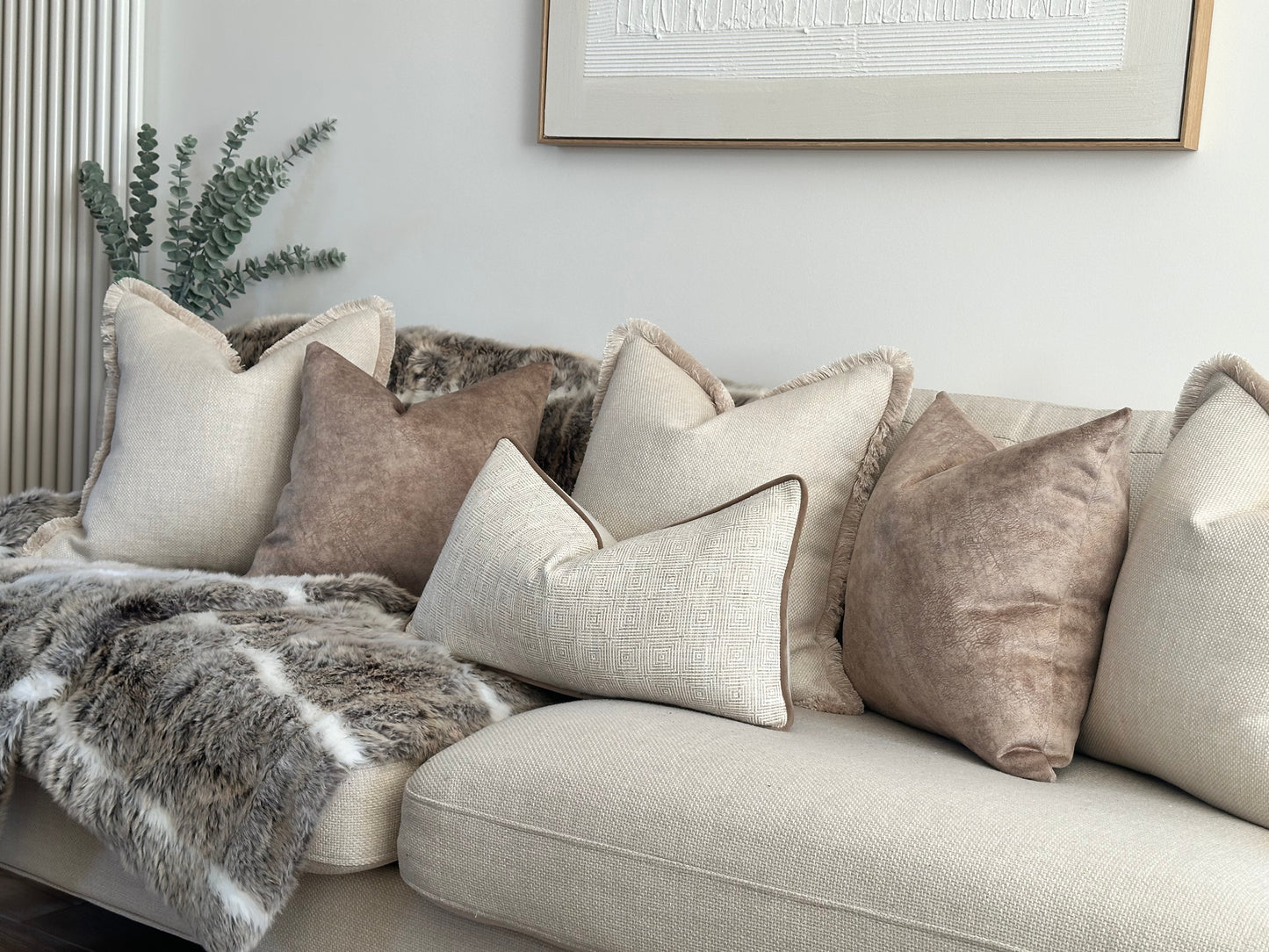 Luxury cushion set on a sofa that includes 3x cream textured cushions with fringe 2 trim beige brown pillows and a geometric patterned rectangle cushion. Perfect for neutral modern home decor