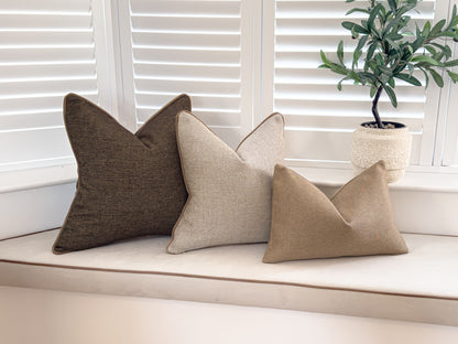 A photo of a neutral cushion combination, it includes a dark brown a textured cream and a rustic beige rectangle cushion.