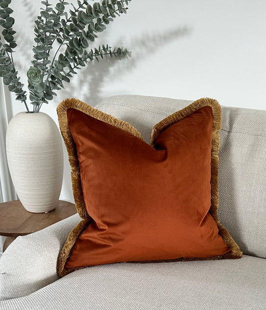 Burnt orange velvet cushion cover with fringe.
