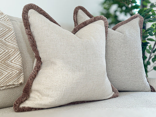 Luxury bespoke cushion in an elegant warm ivory cream hue, crafted from high-end textured fabric and finished with luxurious fringe trim for that designer look.