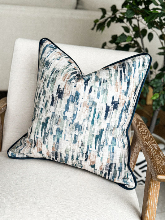 Painterly blue and sage cushion with piped edging on a neutral armchair.”
