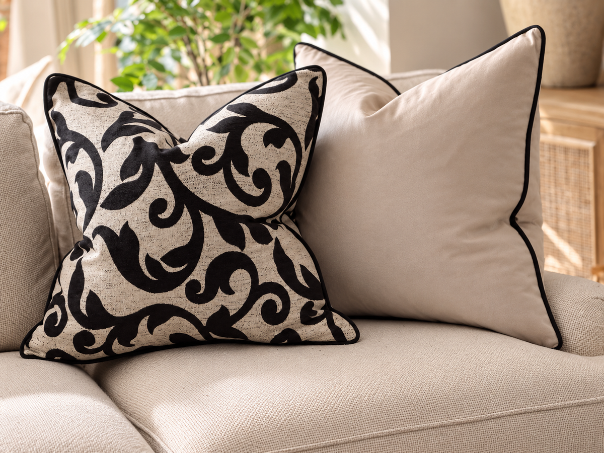 pillow features a black floral pattern on a textured beige background, while the rear pillow is solid beige with black piping.