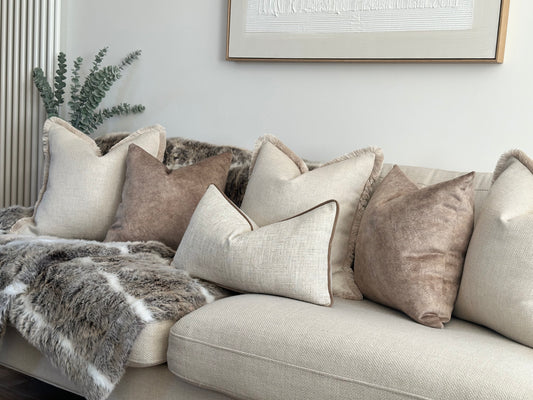 Luxury cushion set on a sofa that includes 3x cream textured cushions with fringe 2 trim beige brown pillows and a geometric patterned rectangle cushion. Perfect for neutral modern home decor 