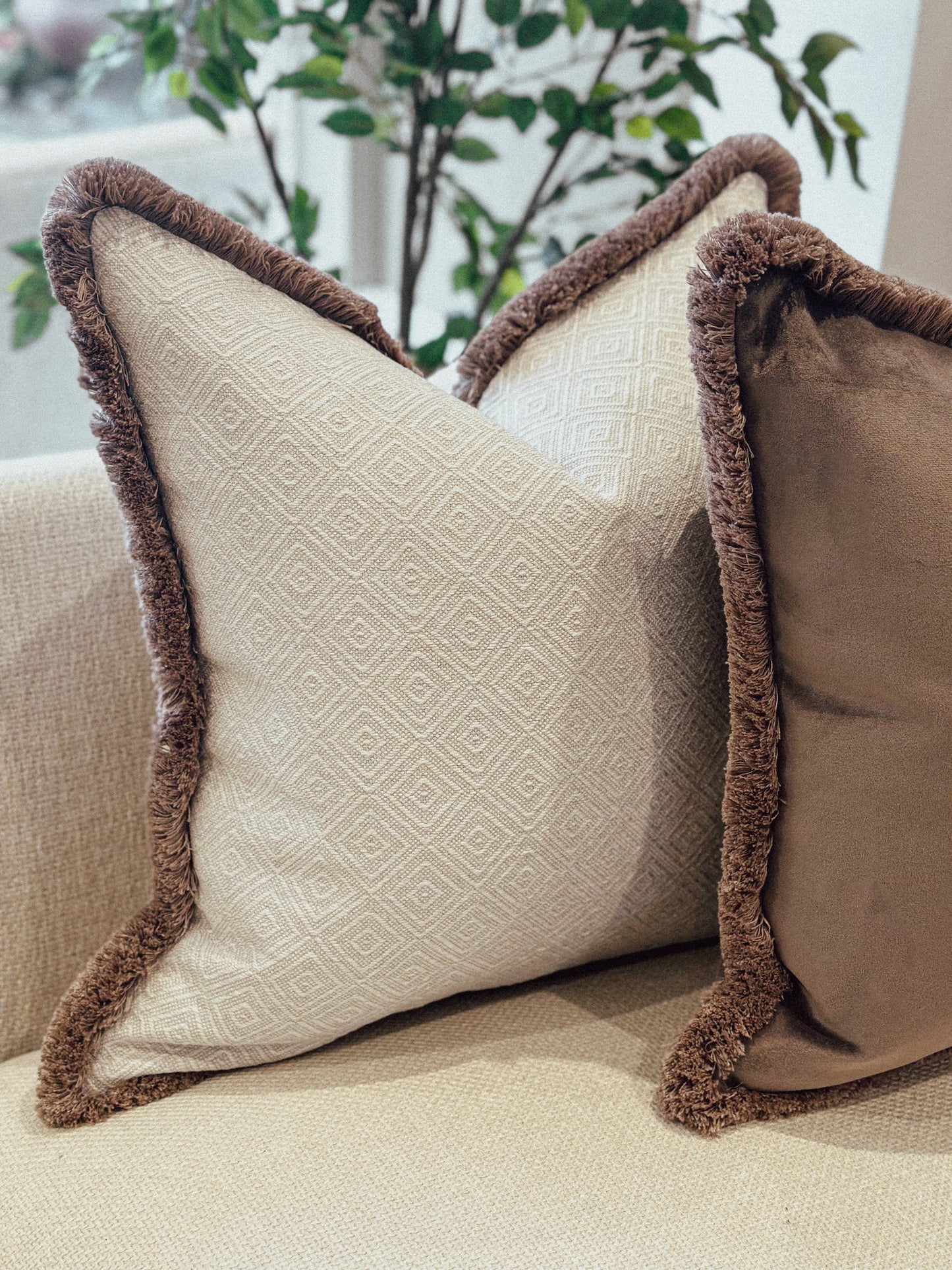 Natural geometric decorative cushion with brown trim on a beige couch.