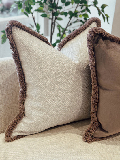 Natural geometric decorative cushion with brown trim on a beige couch.