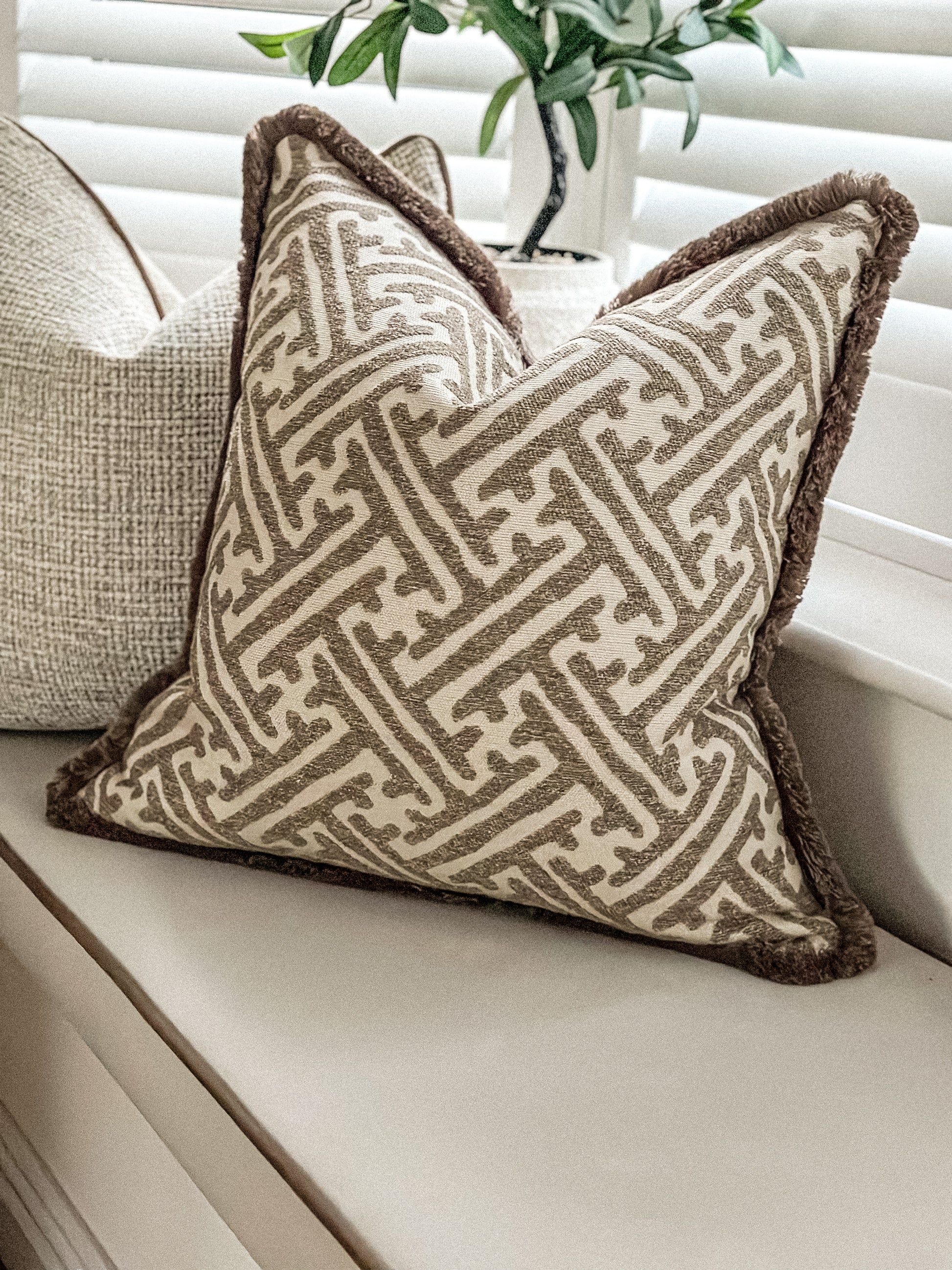 Neutral geometric scatter cushion featuring warm brown fringe and woven stone fabric.