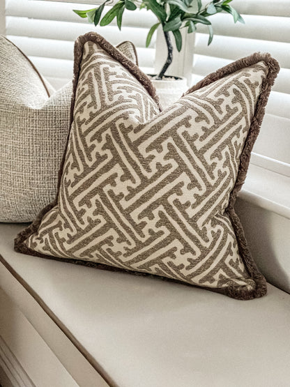 Neutral geometric scatter cushion featuring warm brown fringe and woven stone fabric.