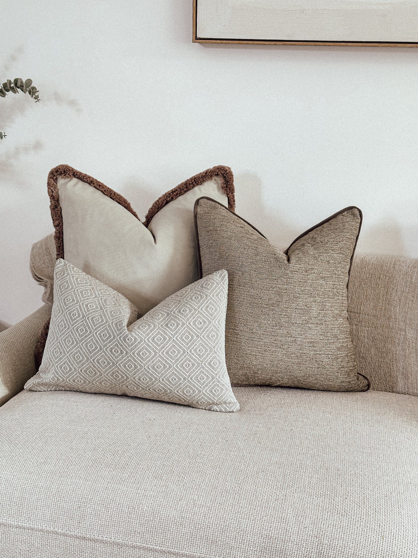 Neutral cushion combo, ivory velvet with beige fringe, textured beige cushion and a cream geometric rectangle pillow.