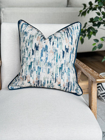 Scatter cushion in soft blue, green, and sand hues with a navy piped trim.