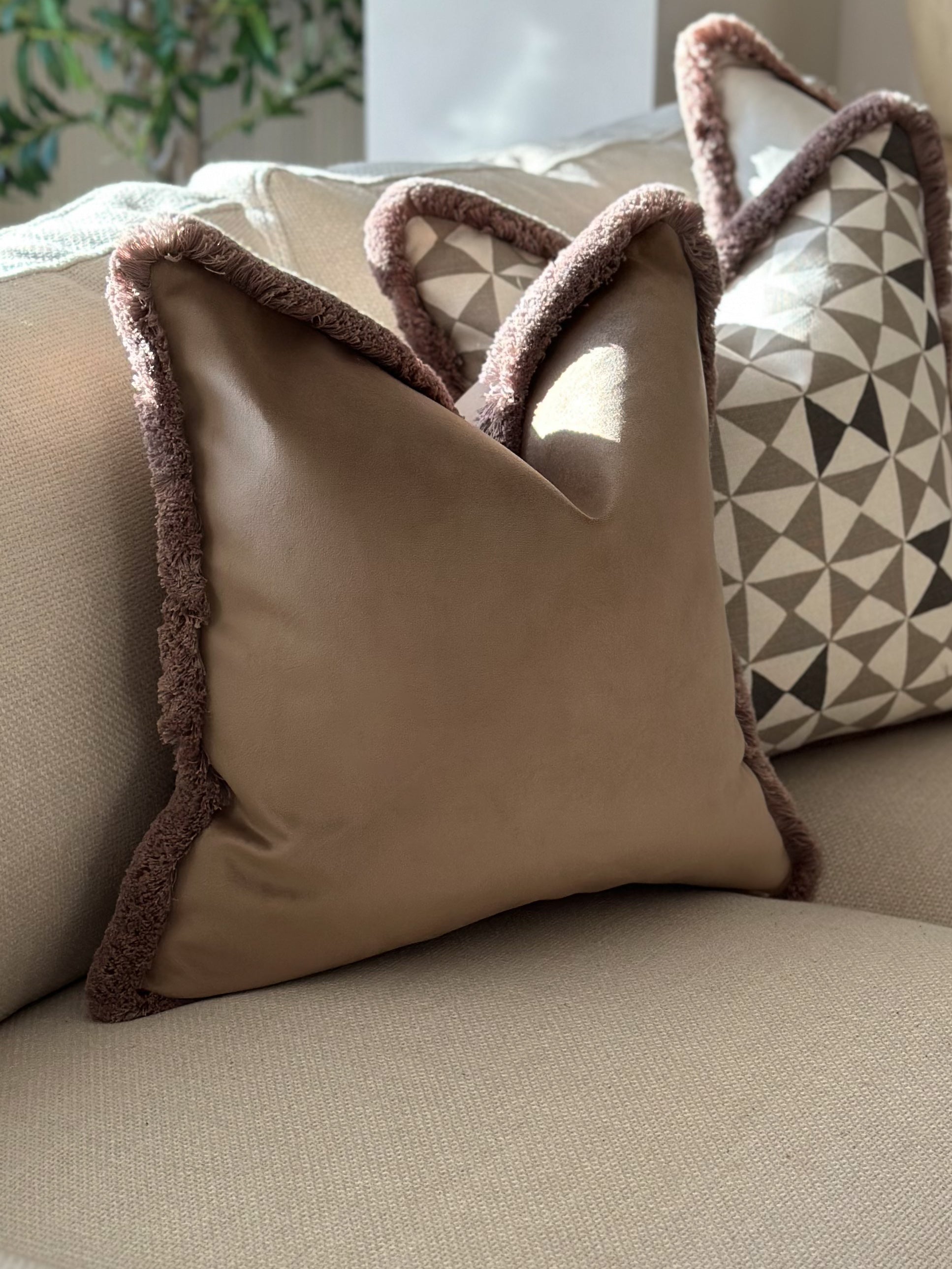 Luxury beige velvet cushion with fringe trim, perfect for neutral home decor. 